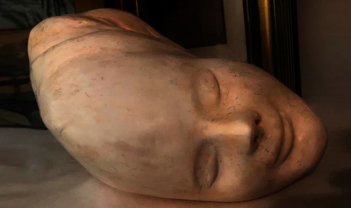 Scultura in gesso di Lalla Vanzella, volto di una giovane donna con gli occhi chiusi e un appena percepito sorriso.