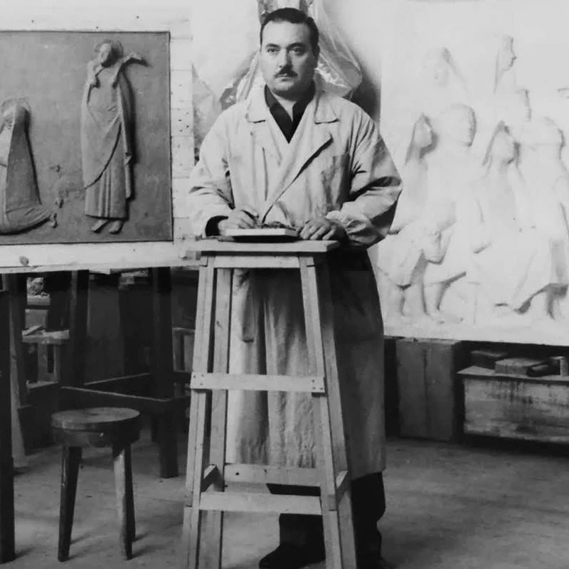Lo scultore Carlo Mandelli all'interno del suo studio, con alle spalle una serie di bassorilievi.