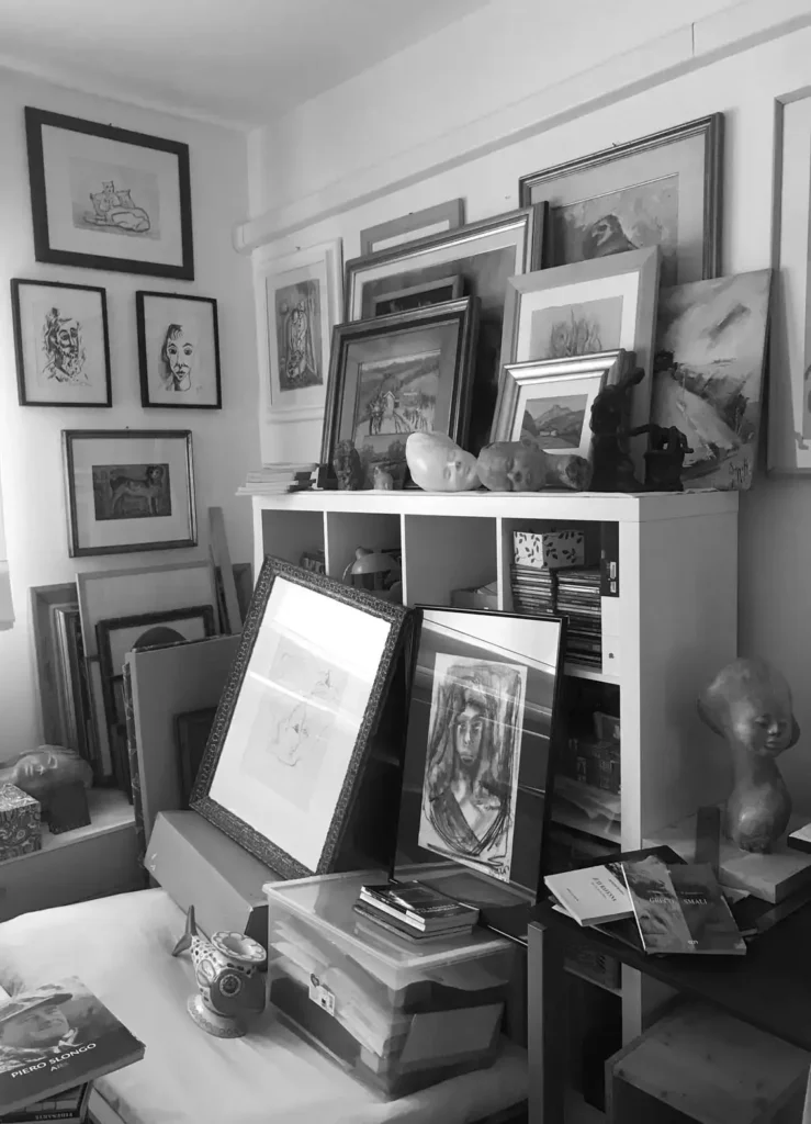 Fotografia in bianco e nero di una stanza a casa mia, in cui moltissime opere, dipinti e sculture attendono ancora una sistemazione definitiva.