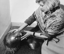 L'artista con una sua scultura Fotografia in bianco e nero con l'artista Lalla Vanzella inginocchiata a terra mentre accarezza la sua scultura in bronzo intitolata: la ferita.